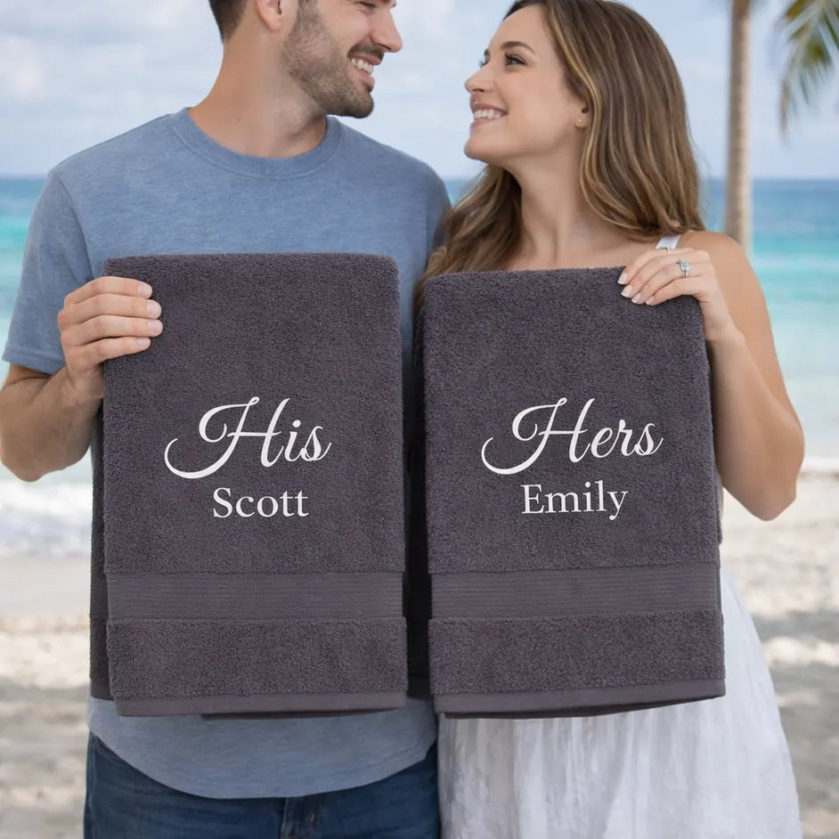 Couple holding personalised His and Hers towels with embroidered names on beach