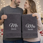 Couple holding personalised Mr and Mrs grey towels with embroidered names in romantic setting