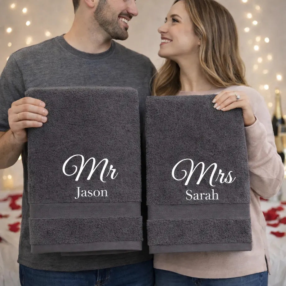 Couple holding personalised Mr and Mrs grey towels with embroidered names in romantic setting