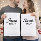 Couple holding personalised white hubby and wifey towels in romantic home setting