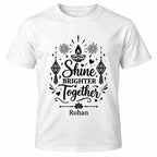 White personalised Diwali T-shirt with black Shine Brighter Together lettering, diya lamps, hanging lanterns, fireworks and custom name beneath