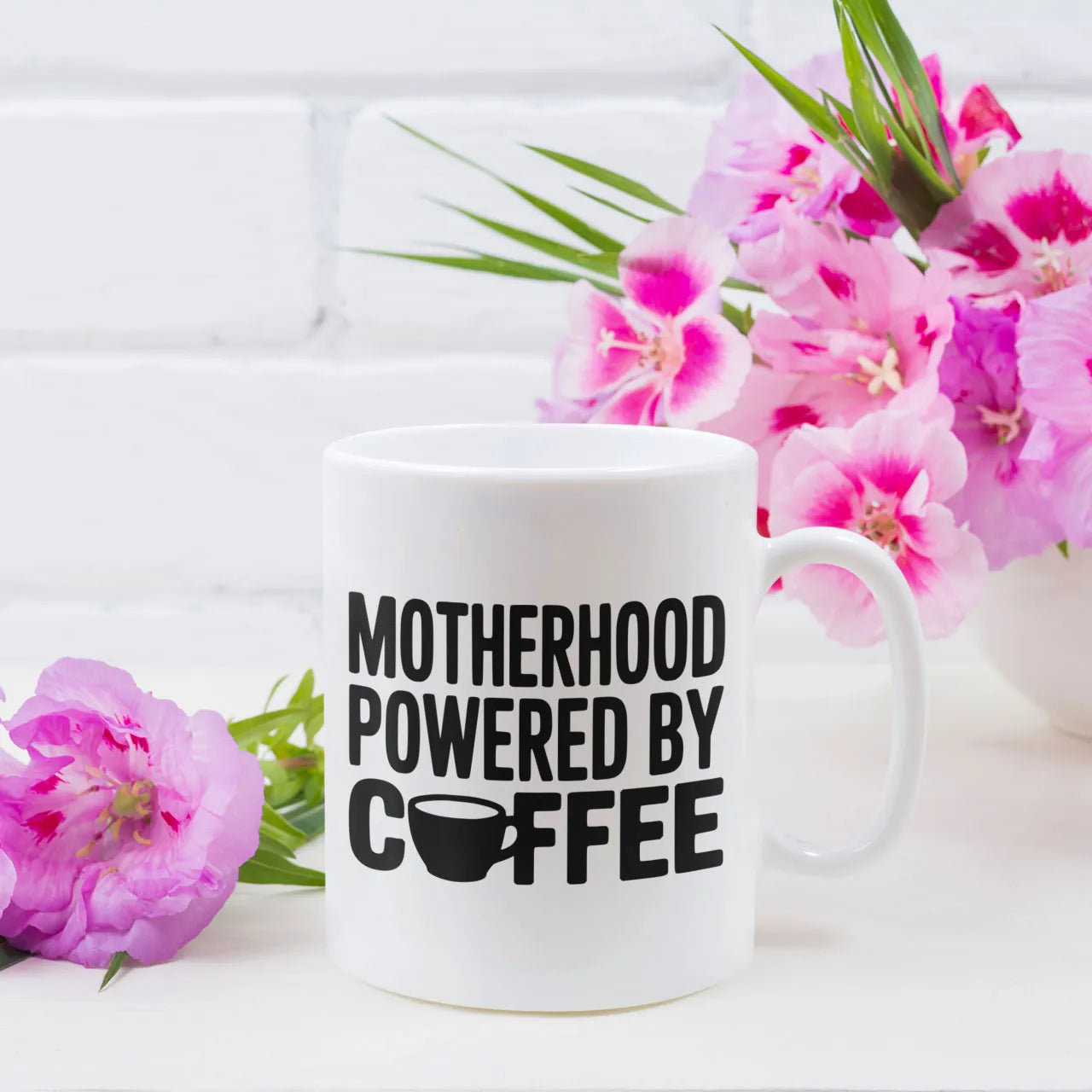 White ceramic mug featuring "Motherhood Powered By Coffee" quote, funny and practical Mother's Day gift for coffee-loving mums, dishwasher safe 11oz cup.