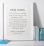 Framed print of wedding vows on a white surface with books and a jar.
